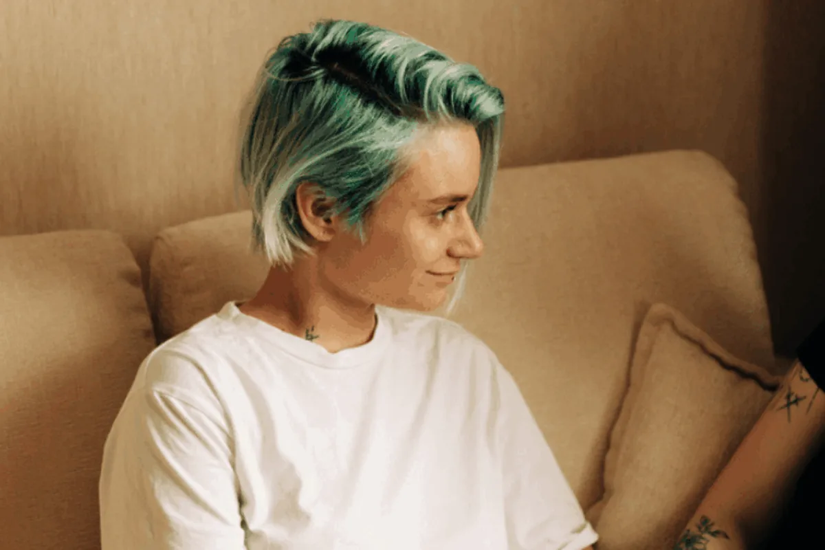 A person with green-tinted hair sitting on a sofa, smiling and looking to the side