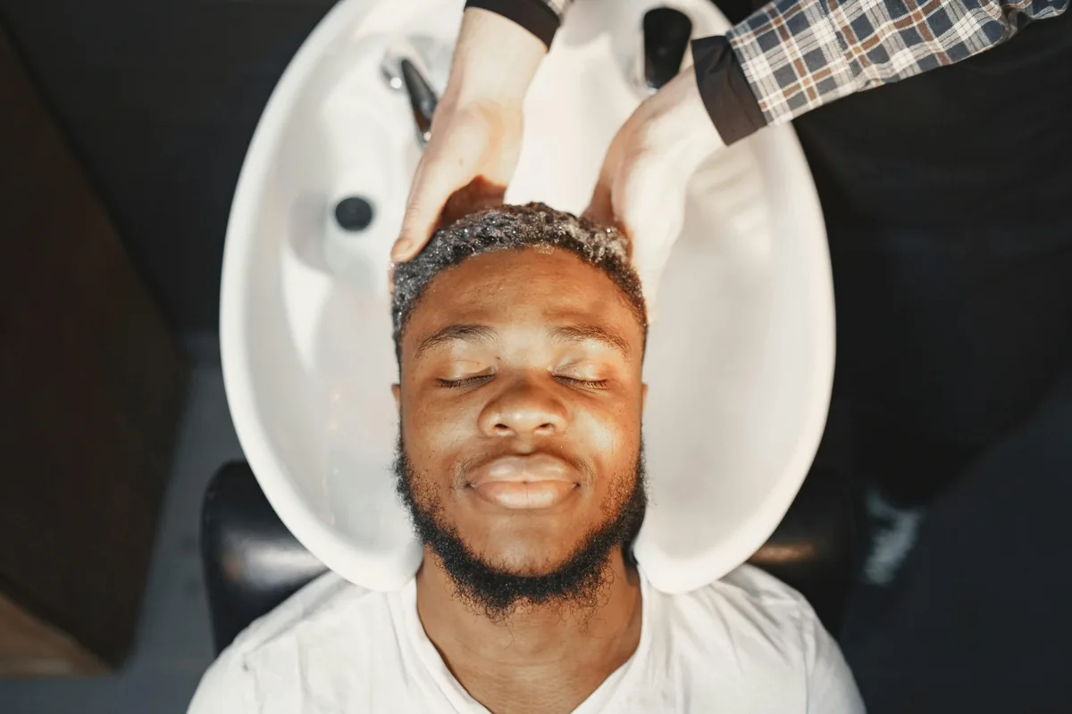 A man leaning his head back into a salon wash basin with his eyes closed while his hair is washed