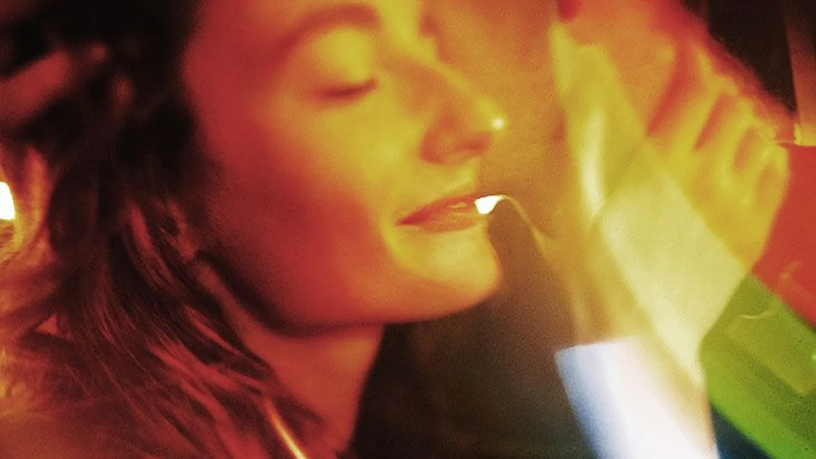 A woman with her eyes closed bathed in warm orange and rainbow light
